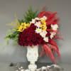 Large floral arrangement in a white sculptural vase with red, yellow, and white blooms