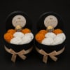 Two black round gift boxes with white and orange roses and gold chocolates