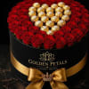 Red roses arranged around gold-wrapped chocolates in a black round box