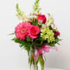 Pink gerbera daisies and roses in a clear glass vase with a pink ribbon