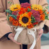 Bouquet of sunflowers, orange roses, and burgundy blooms wrapped in kraft paper