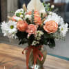 Peach roses and white daisies arranged in a glass vase with a red ribbon