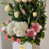 Pink roses, white hydrangea, and pink orchids arranged in a white box