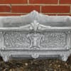 Ornate gray stone planter box against a brick wall