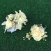 Two ivory rose corsages with small white flowers on green turf