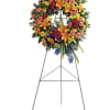 Large standing floral wreath on an easel with orange lilies and mixed blooms