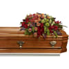 Casket spray with red and peach flowers on a wooden casket