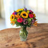 Mixed bouquet of sunflowers, roses, and lilies in a glass vase