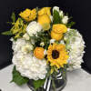 Yellow roses and sunflowers arranged with white hydrangeas in a black vase