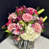 Pink and white floral arrangement in a round vase with a striped ribbon