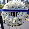 White floral funeral wreath on an easel with a blue ribbon
