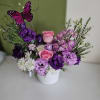 Purple and pink flower arrangement in a white pot with a butterfly pick