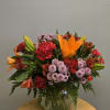 Mixed bouquet of orange lilies, red carnations, and purple mums in a glass vase