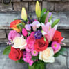Colorful arrangement of roses, lilies, tulips, and mixed blooms in a clear glass vase