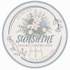 Circular sign with a floral standing spray illustration and the word Sunshine