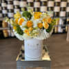 Yellow and white floral arrangement in a white hat box