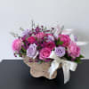 Pink and lavender roses in a woven basket with a ribbon bow