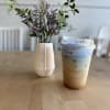 Small purple flower arrangement in a white vase beside an iced drink