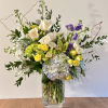 Mixed bouquet of white, yellow, purple, and blue flowers in a glass vase