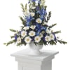 Tall blue and white floral arrangement in a white urn on a pedestal