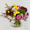 Mixed bouquet of pink, yellow, and purple flowers in a clear glass vase