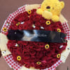 Heart-shaped bouquet of red roses with a yellow teddy bear and birthday ribbon