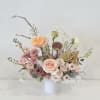 Asymmetrical arrangement of peach and blush flowers in a white cylinder vase