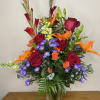 Mixed bouquet of red roses, orange lilies, and purple daisies in a clear vase
