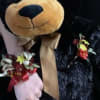 Teddy bear holding small floral accents and a ribbon