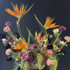 Large mixed floral arrangement with orange bird-of-paradise and pink blooms in a gold vase
