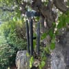 Black wind chimes hanging from a tree branch in a garden