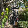 Black memorial wind chime hanging outdoors among trees and shrubs