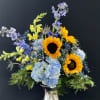 Mixed bouquet with sunflowers, blue hydrangea, and purple flowers in a silver vase