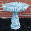 Stone birdbath with rose relief against a brick wall