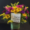 Bright yellow daisies, pink tulips and purple accents in a clear glass