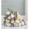 Cremation urn surrounded by white roses, white mums, and purple flowers in a crescent arrangement