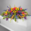 Colorful floral casket spray with sunflowers, roses, and purple blooms
