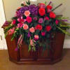 Large mixed floral arrangement with red roses and purple blooms in a wooden casket spray