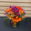 Colorful bouquet of roses, alstroemeria, and purple daisies in a glass vase with an orange ribbon