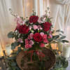 Red and pink rose arrangement in a glass vase with candles and draped fabric