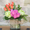 Pink roses and orange tulips in a glass vase with burlap ribbon