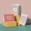 Three greeting cards on stacked boxes, including spring, thank you, and birthday designs.