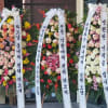 Three tall floral standing wreaths with white ribbon banners and mixed blooms