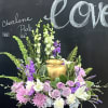 Lavender roses and pink flowers arranged around a gold urn