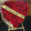 Heart-shaped red rose arrangement on an easel with a gold LOVE sash
