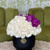 White rose arrangement with purple orchids in a black vase