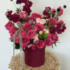 Pink and magenta roses arranged in a round box with ribbon.