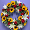 Circular wreath of red roses, white lilies, and yellow sunflowers on a stand