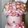Pink and blush roses arranged in a round pink hat box with a ribbon bow.