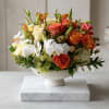 Mixed bouquet of roses, orchids, and lilies in a white pedestal bowl